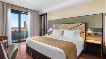 A hotel room with a large bed, a desk, a chair, a nightstand, and a view of the city.
