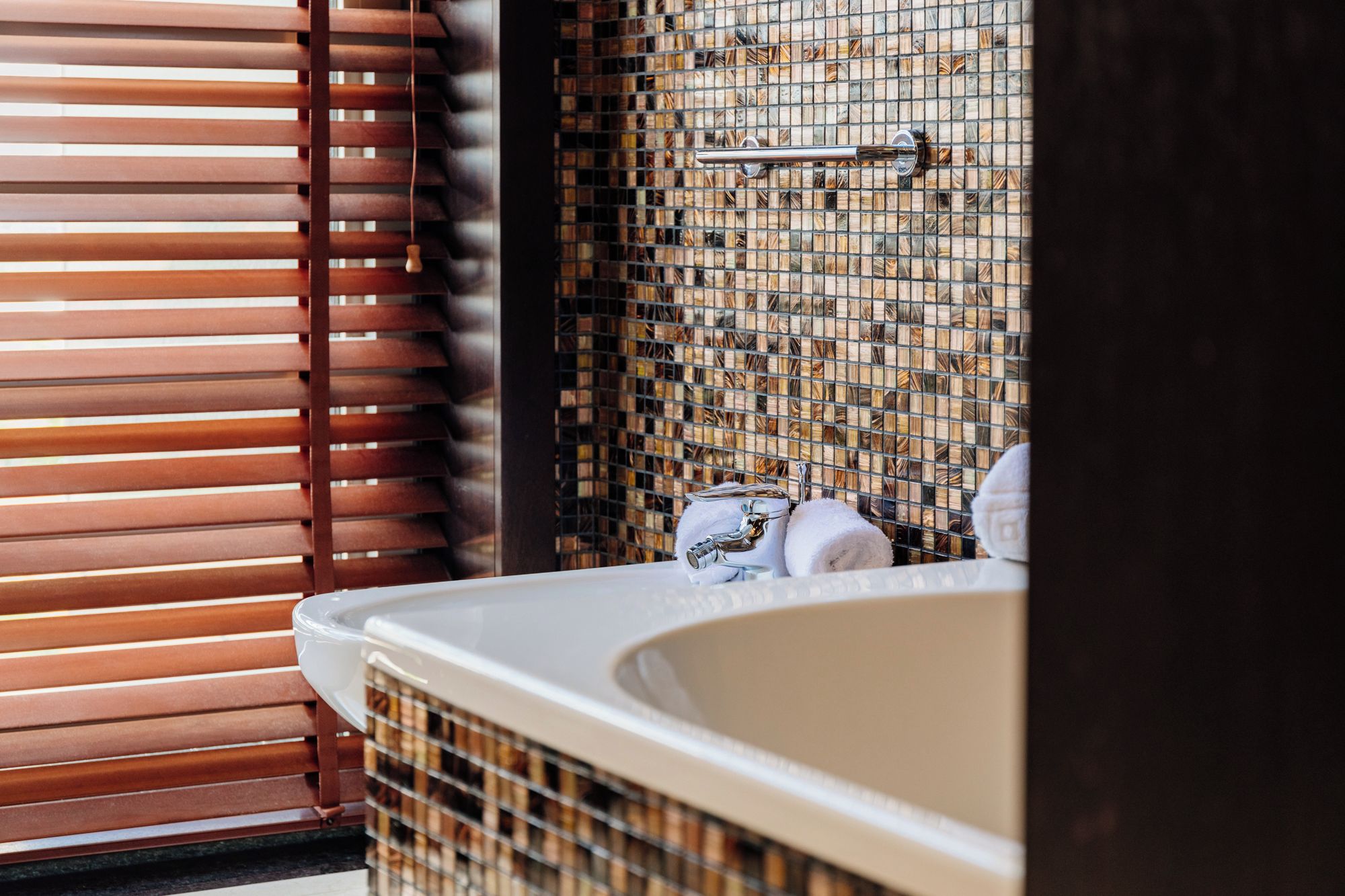 Une salle de bain avec une baignoire, une serviette et un mur orné d’un motif en mosaïque.
