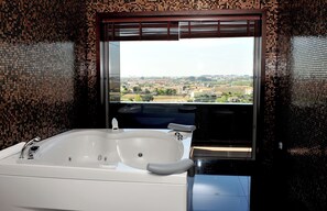 A bathroom with a large bathtub, a window with a view of a cityscape, and mosaic tile walls. - Axis Porto Business & Spa Hotel (Matosinhos)