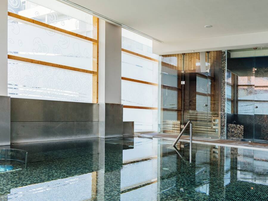 Un área de piscina interior moderna con paredes de vidrio, piso pulido y una escalera que sube a niveles superiores.