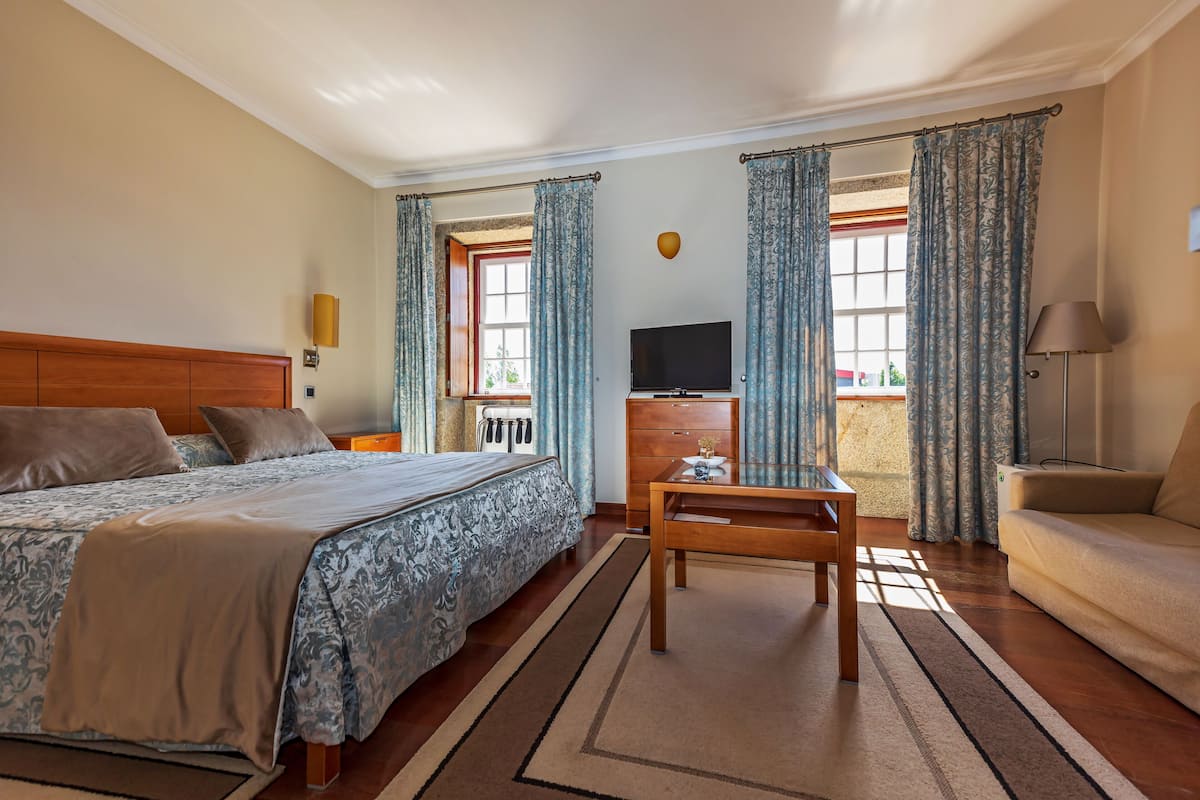 A hotel room with a bed, a desk, a television, and a sofa.