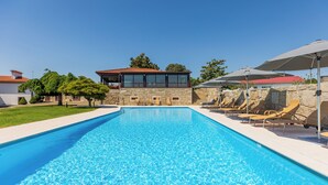 A swimming pool with lounge chairs and umbrellas, a stone wall, and a building with a red roof. - Hotel Rural Quinta de S Sebastiao (Viana do Castelo)