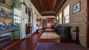 A hallway with a wooden ceiling, stone walls, and blue and white ceramic plates on the left. There are chairs and a small table with a plant on the right. - Hotel Rural Quinta de S Sebastiao (Viana do Castelo)