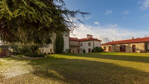 A traditional stone building with a red-tiled roof, a courtyard with cobblestone paving, and mature trees. - Hotel Rural Quinta de S Sebastiao (Viana do Castelo)