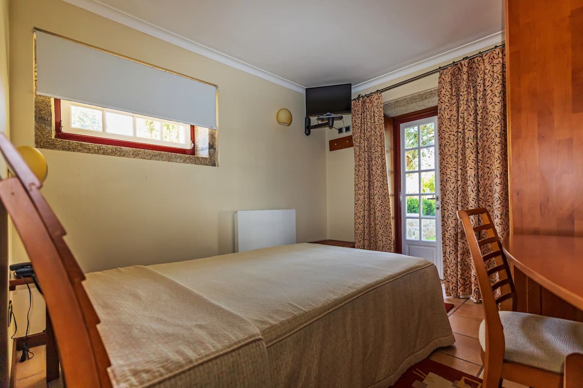 A room with a bed, a chair, a television mounted on the wall, a window with curtains, and a door.