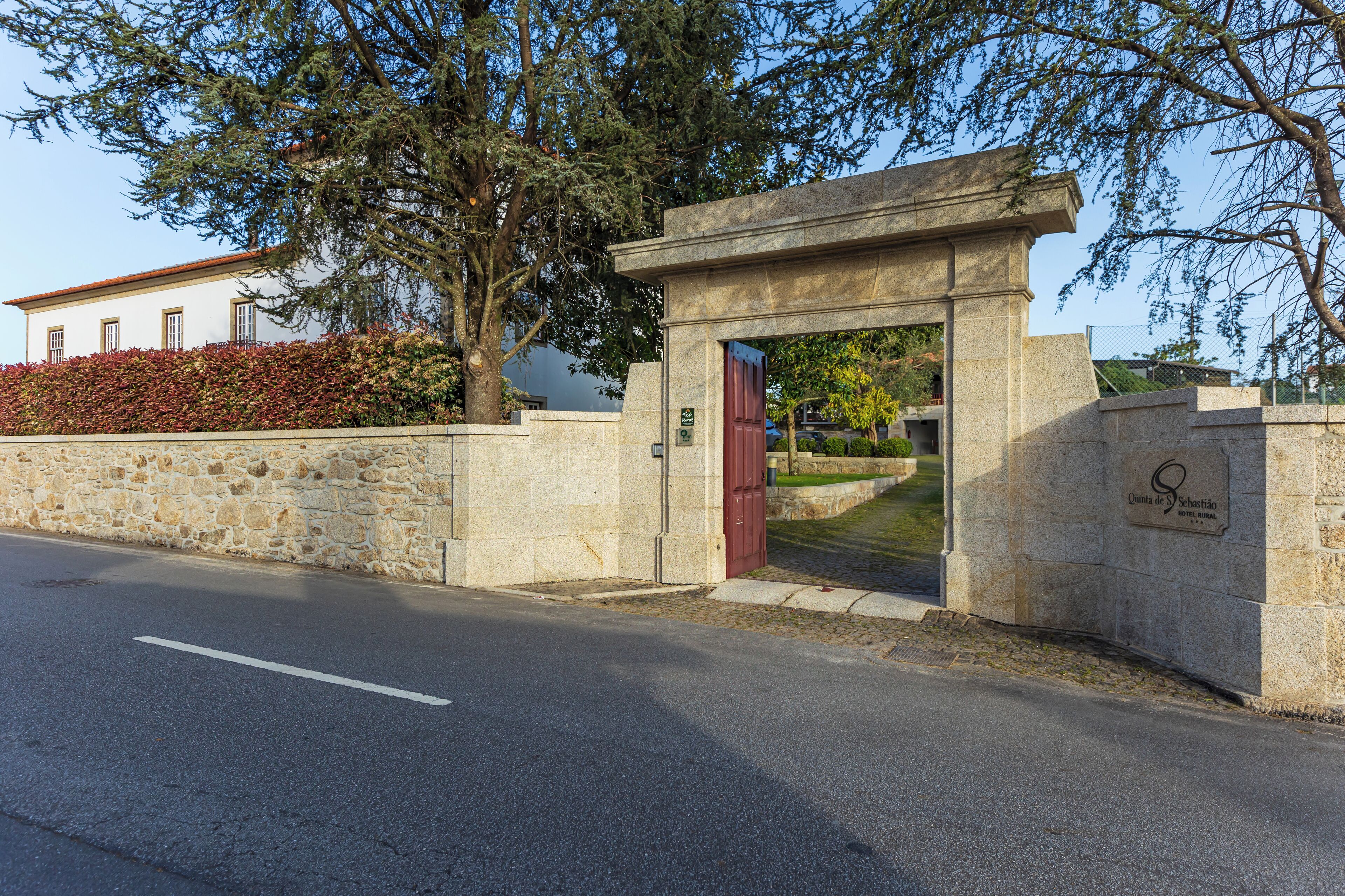 A stone entrance gate with a red door, a stone wall, and a building in the background.