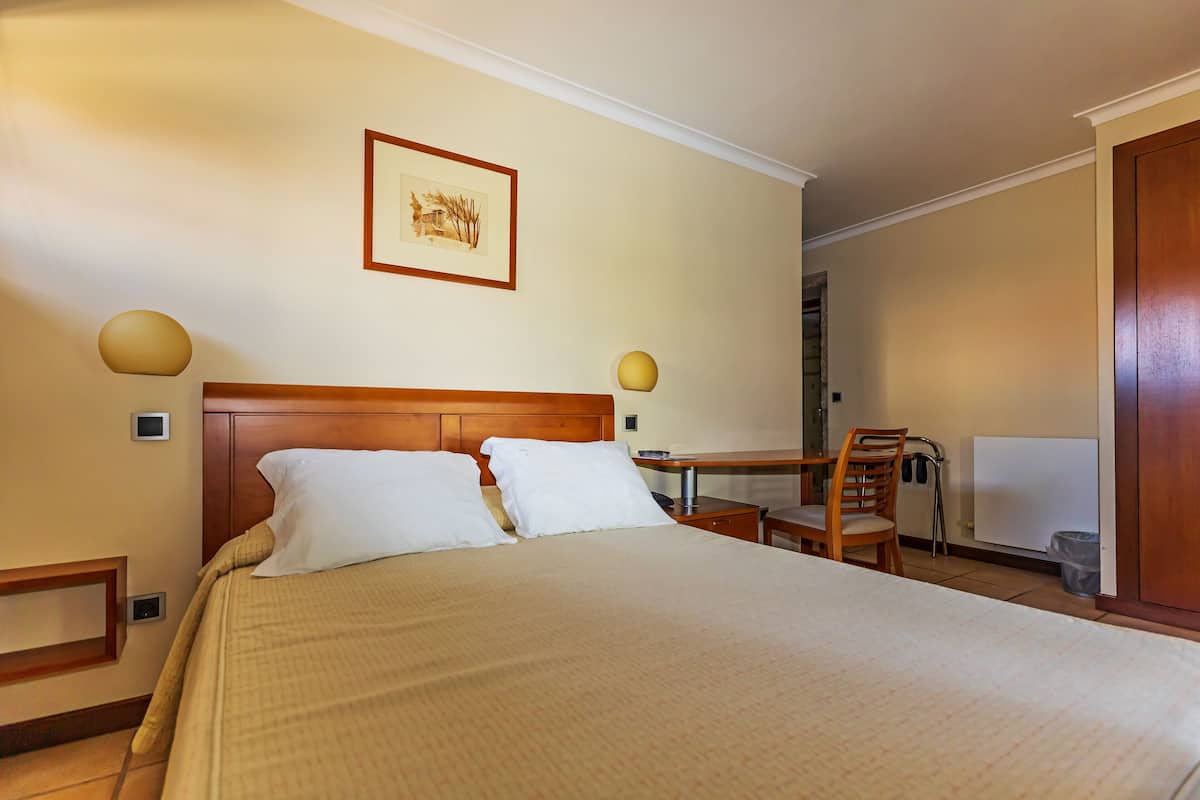 A hotel room with a large bed, a wooden headboard, a desk with a chair, and a framed picture on the wall.