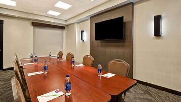 A conference room with a long wooden table, chairs, water bottles, and a flat-screen TV mounted on the wall.