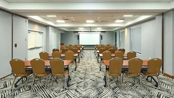 A conference room with rows of tables and chairs, a projector screen, and a patterned carpet.