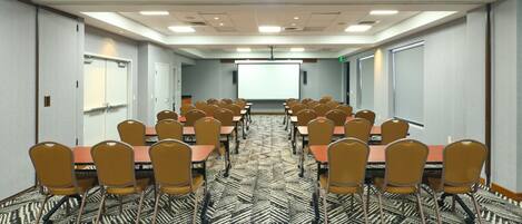 A conference room with rows of tables and chairs, a projector screen, and a patterned carpet.