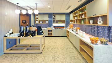 A modern cafe with a counter, coffee machines, and a variety of food items displayed.