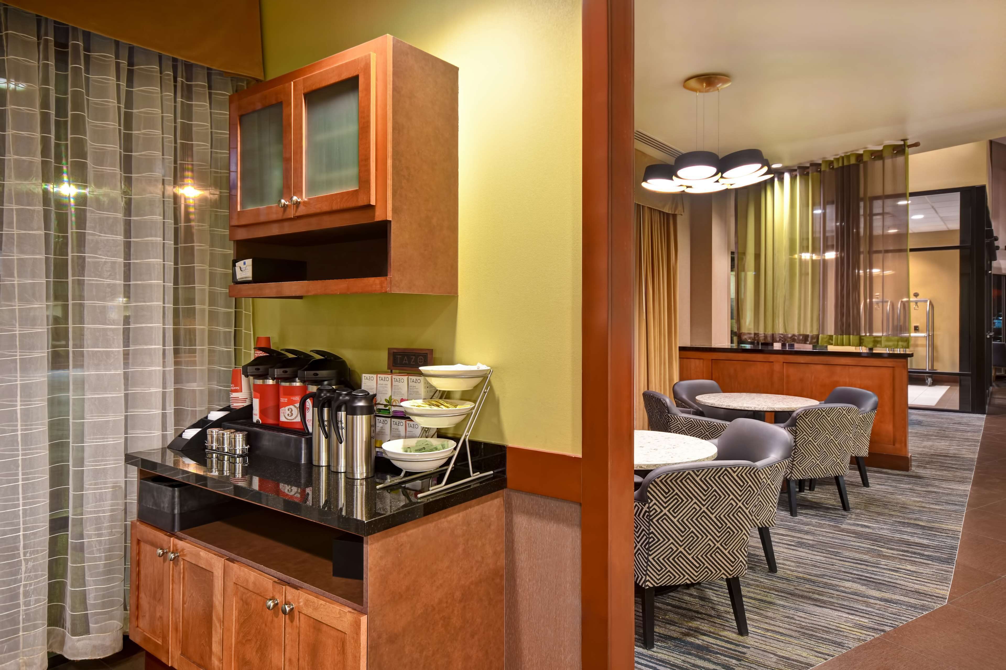 Una habitación de hotel con kitchenette, una zona de comedor con sillas, un bar y un amplio ventanal con cortinas.