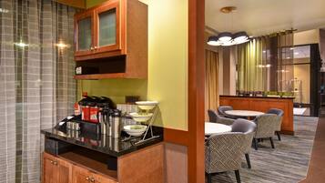 A hotel room with a kitchenette, a dining area with chairs, a bar, and a large window with curtains.