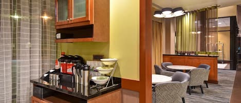 Una habitación de hotel con kitchenette, una zona de comedor con sillas, un bar y un amplio ventanal con cortinas.