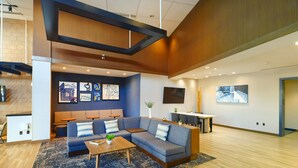 A modern lounge area with a sectional sofa, a coffee table, and a small side table. There is a flat-screen TV mounted on the wall and a potted plant on a side table.