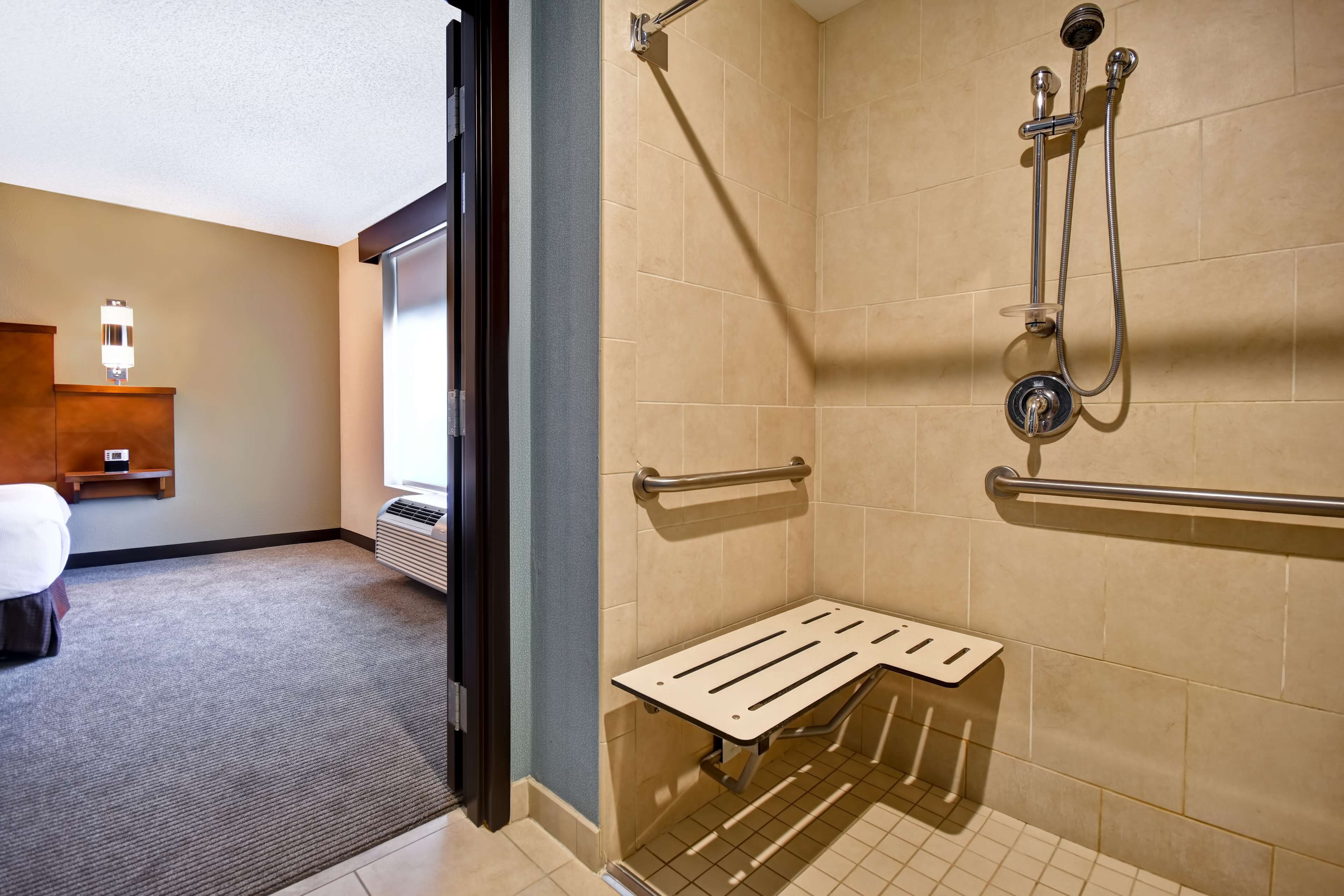 Ein Hotelbad mit Dusche, Haltegriffen, Toilette und kleinem Waschbecken.