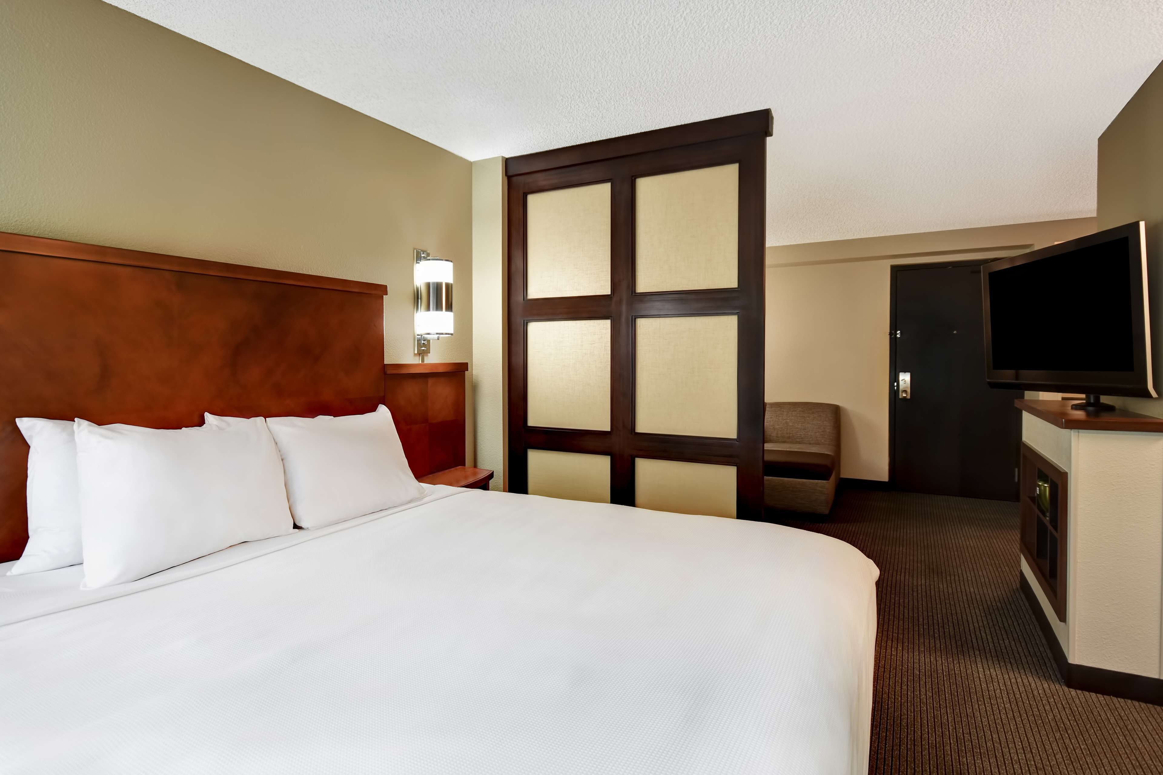 A hotel room with a large bed, a wooden headboard, a television, and a door with a glass panel.