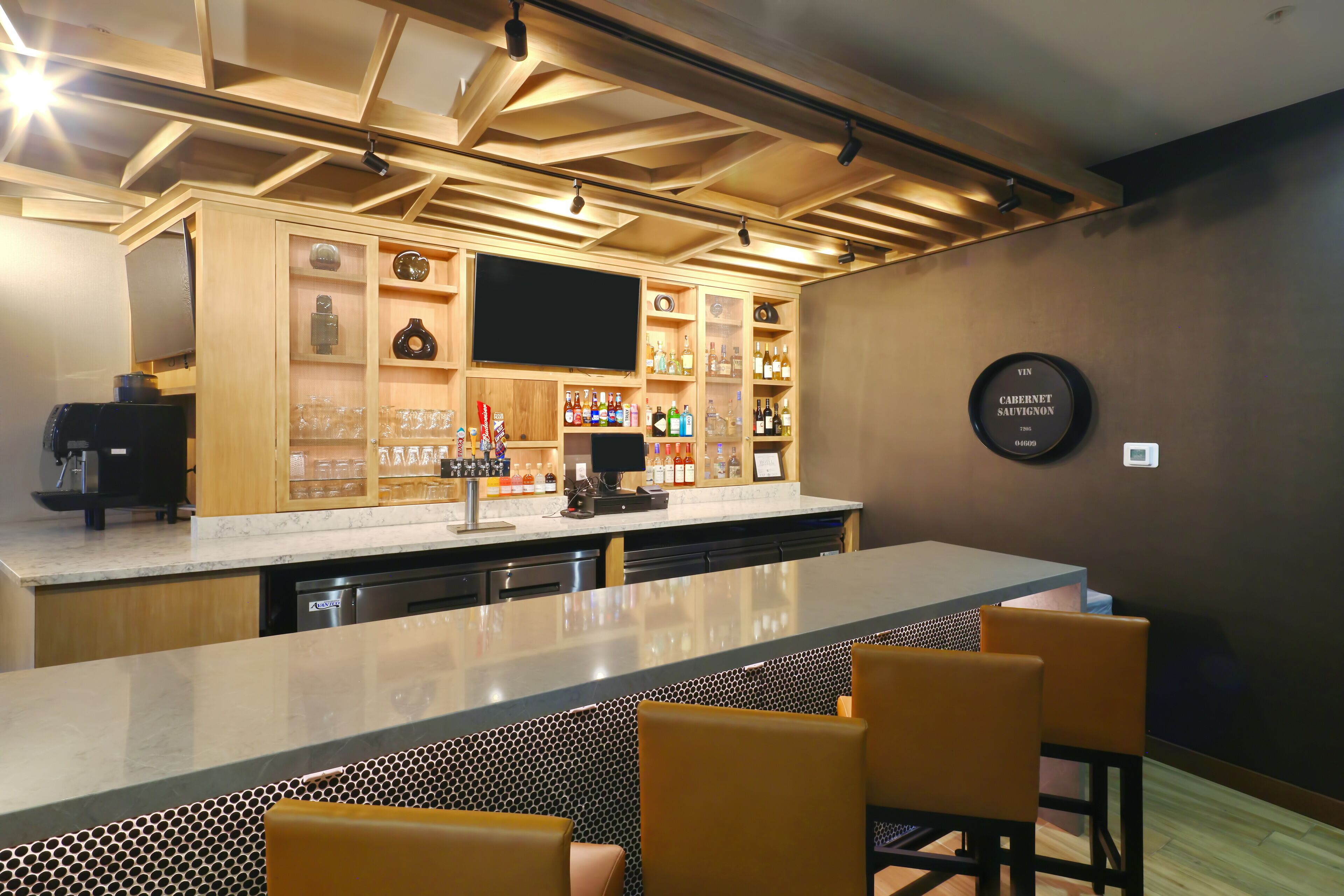 A bar area with a long counter, bar stools, a television, and shelves with bottles and glasses.