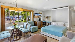 A hotel room with a bed, seating area, TV, and a view of the street. - The Gardens at West Maui (Lahaina)