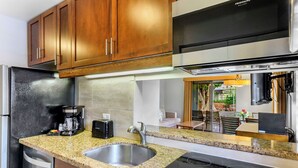 A modern kitchen with granite countertops, stainless steel appliances, and wooden cabinets. - The Gardens at West Maui (Lahaina)