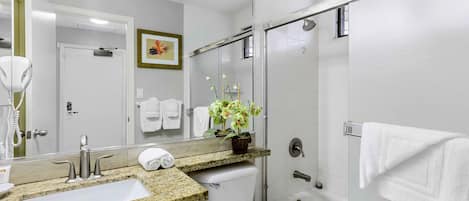 A modern bathroom with a granite countertop sink, a toilet, a shower with a glass door, and a mirror with a framed picture.