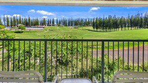 A balcony with a view of a golf course, a building with a sloped roof, and a fence. - The Gardens at West Maui (Lahaina)