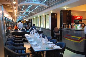 A restaurant with long tables, chairs, and a Coca-Cola branded counter. - Ohris Baseraa Inn (Hyderabad)