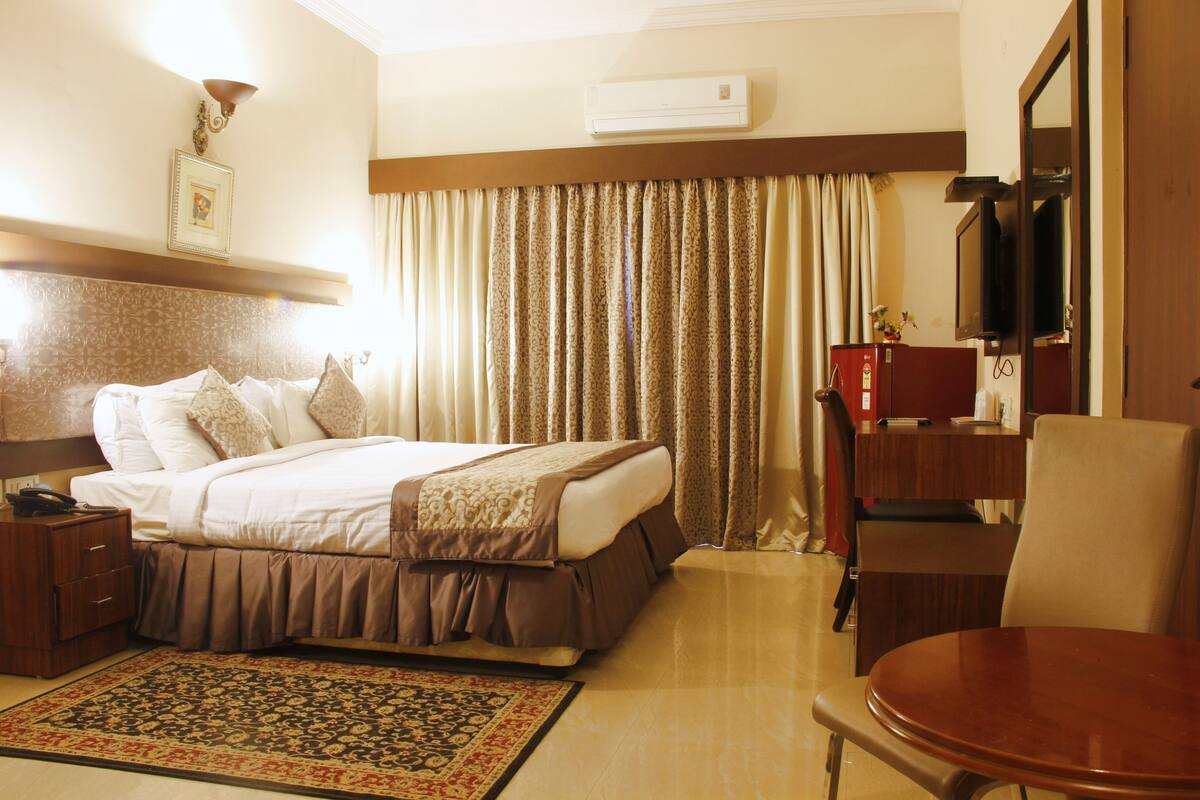 Een hotelkamer met een bed, een bureau, een stoel, een televisie en een groot raam met gordijnen.