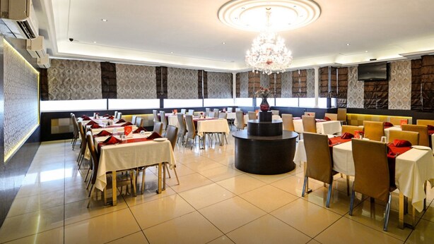 Un vaste espace dédié à la salle à manger, avec de nombreuses tables et chaises, une table ronde centrale et un lustre.