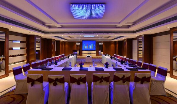 A conference room with a long table, chairs with bows, and a presentation screen in the background.
