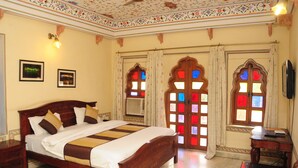 A traditional room with a wooden bed, a desk, and decorative windows. - Hotel Sajjan Niwas (Jaipur)