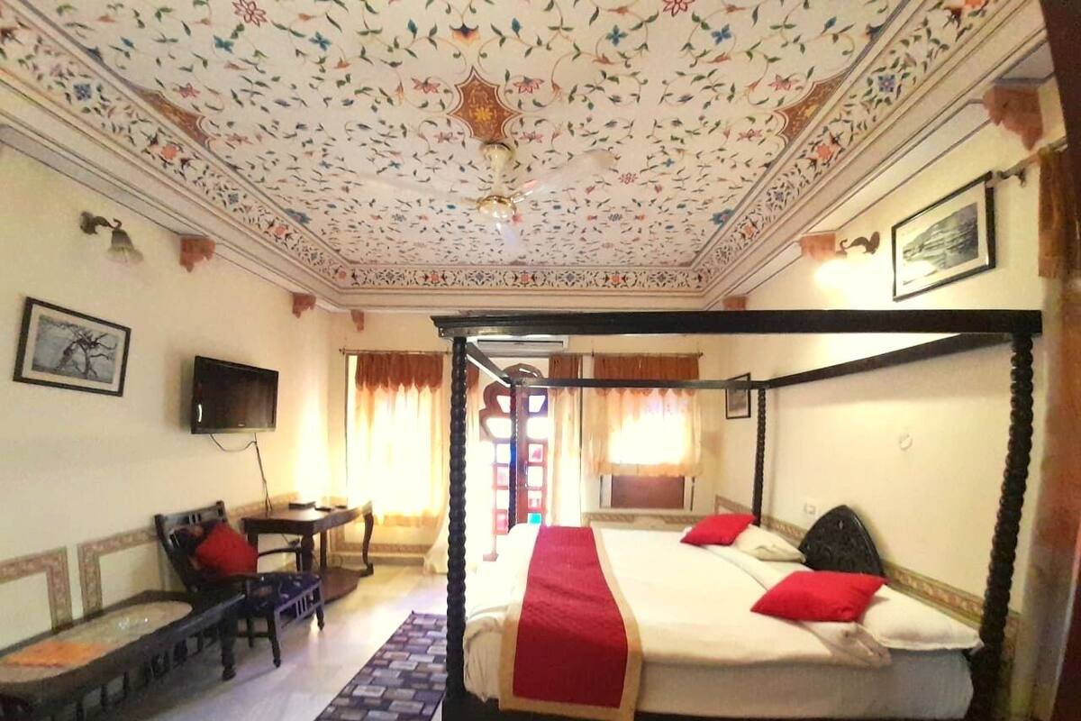 Un lit à baldaquin avec des oreillers rouges, un téléviseur fixé au mur et un plafond orné de motifs.