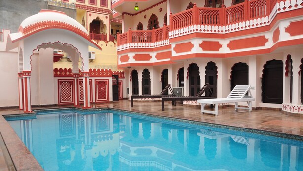 A swimming pool with a reflection of architectural details, surrounded by a building with balconies and arched doorways. - Hotel Sajjan Niwas (Jaipur)