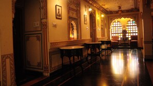A corridor with ornate wall decorations, a polished floor, and a series of small tables and chairs. - Hotel Sajjan Niwas (Jaipur)