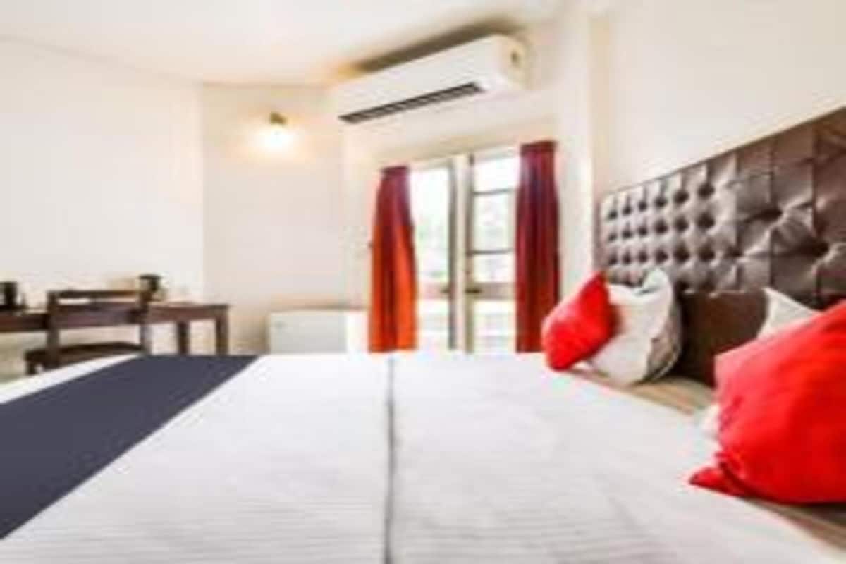 Ein Hotelzimmer mit einem großen Bett, einem Kopfteil, einem Schreibtisch und einem Fenster mit Vorhängen.