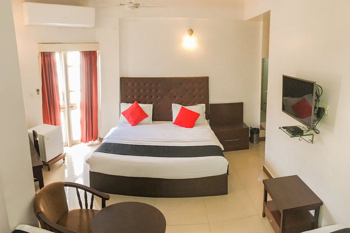 Ein Hotelzimmer mit einem großen Bett, zwei Nachttischen, einem an der Wand montierten Fernseher, einem kleinen runden Tisch und einem Sessel.