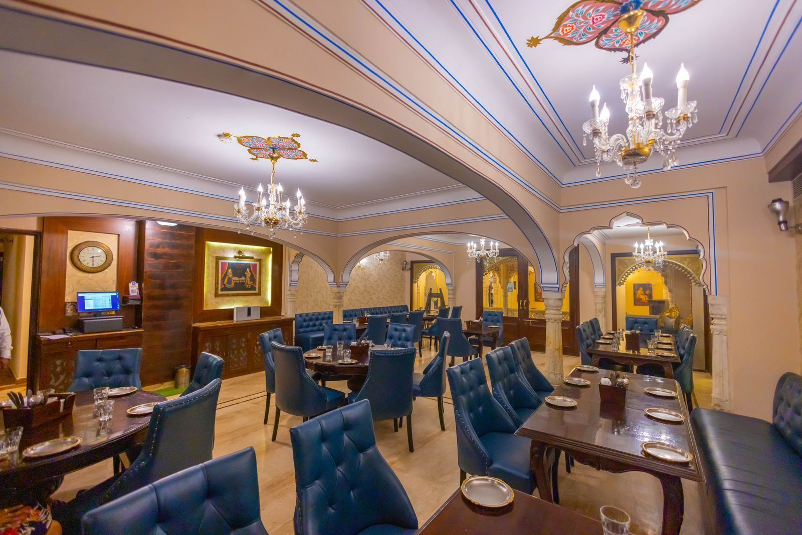 A luxurious dining area with high-backed blue chairs, ornate chandeliers, and a classic interior design.