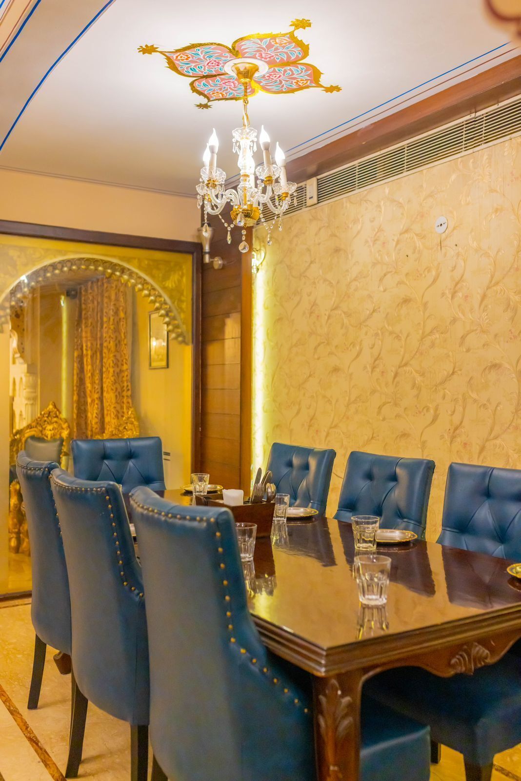 Uma sala de jantar com uma grande mesa de madeira, cadeiras estofadas em azul e um lustre.