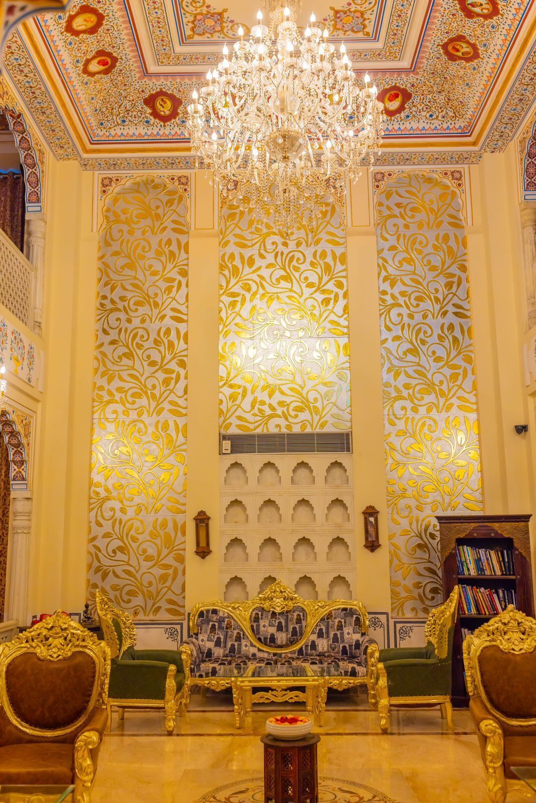 Um quarto luxuoso com um grande candelabro, detalhes ornamentais nas paredes e mobiliário tradicional.