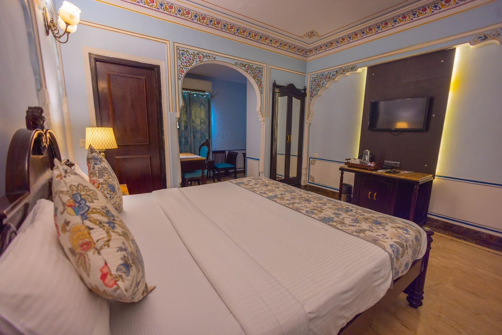 A hotel room with a large bed, a TV, a desk, and a mirror.
