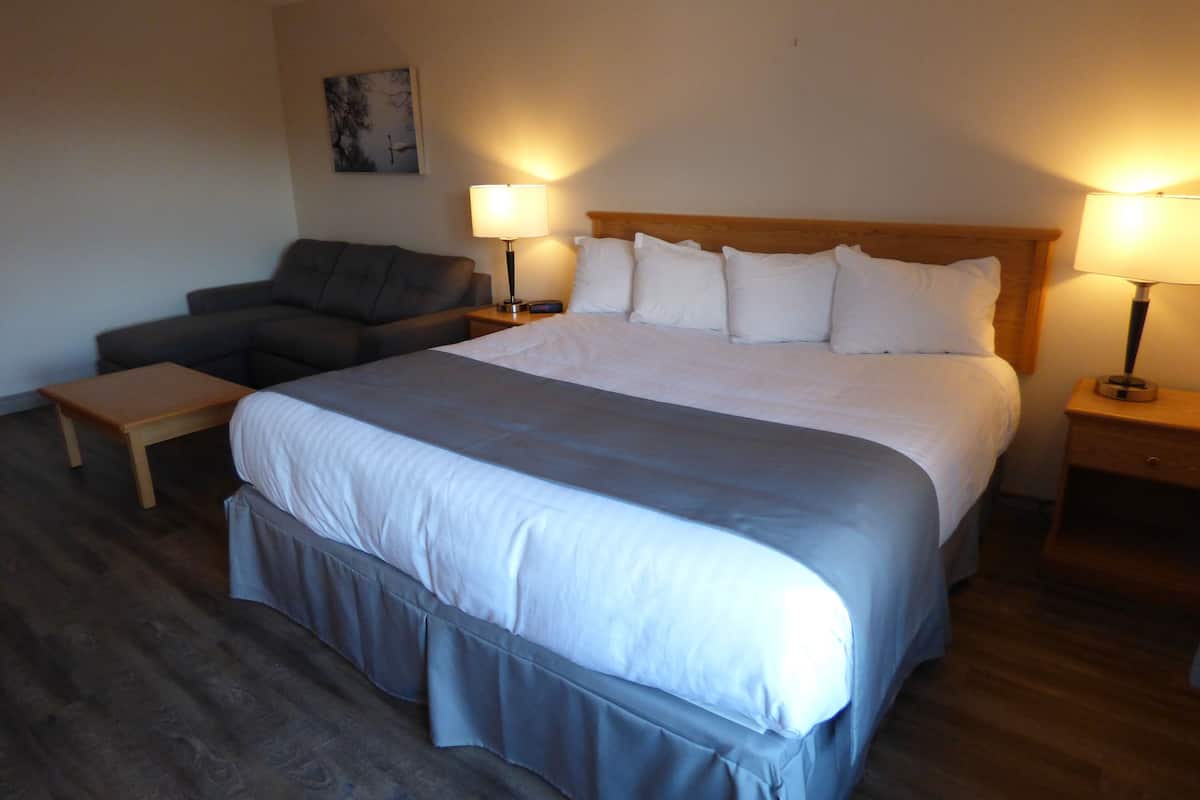 Une chambre d’hôtel avec un grand lit, deux tables de chevet avec des lampes, un canapé gris et une petite table en bois.