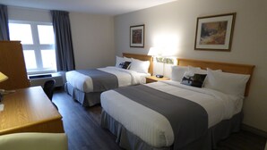 Una habitación de hotel con dos camas, un escritorio, una silla y un ventanal con cortinas.