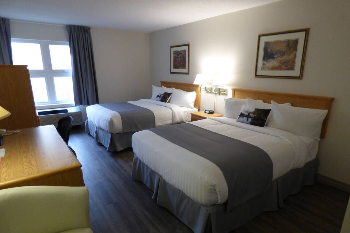 Une chambre d’hôtel avec deux lits, un bureau, une chaise et une fenêtre avec des rideaux.