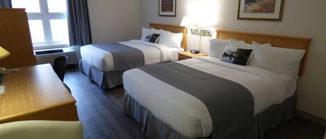 A hotel room with two beds, a desk, a chair, and a window with curtains.