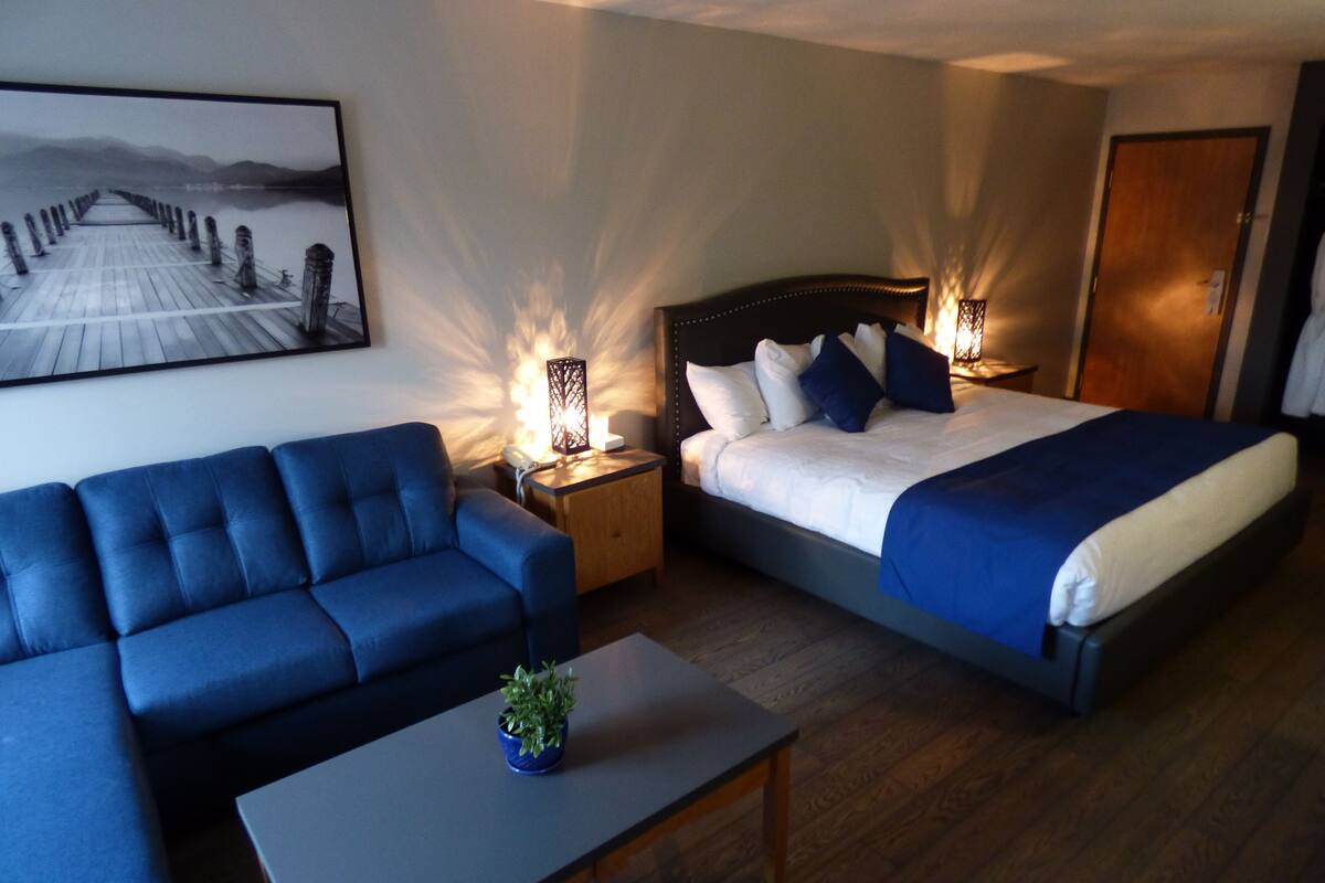Une chambre d’hôtel avec un lit, un canapé bleu, une petite table et une table de chevet avec une lampe.