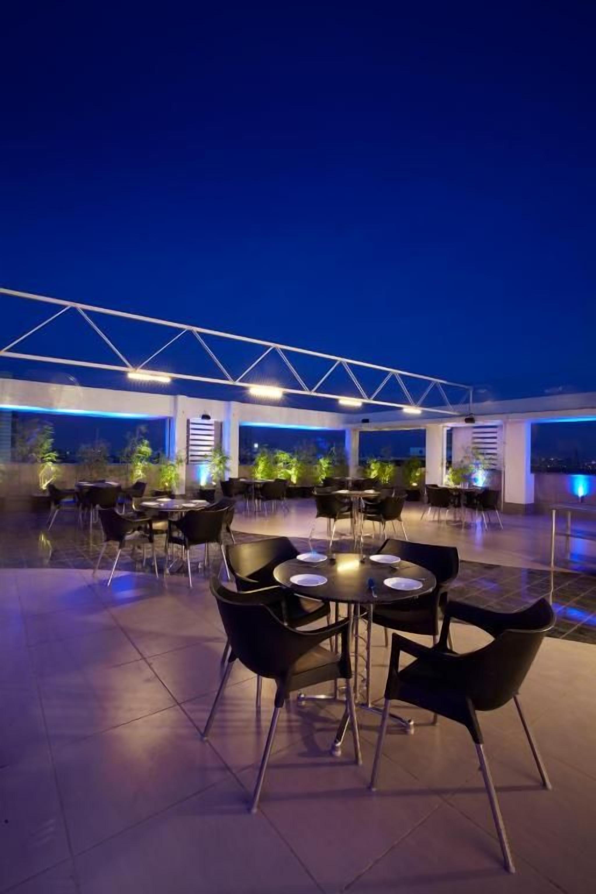 An outdoor dining area with tables and chairs, under a covered structure with a truss design.