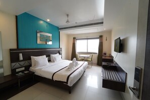 Une chambre d’hôtel avec un grand lit, un bureau doté d’un téléviseur à écran plat, une fenêtre avec des rideaux et un ventilateur de plafond.