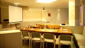 Un salón de conferencias con mesas, sillas, una pantalla de proyector y un muro con diseño.