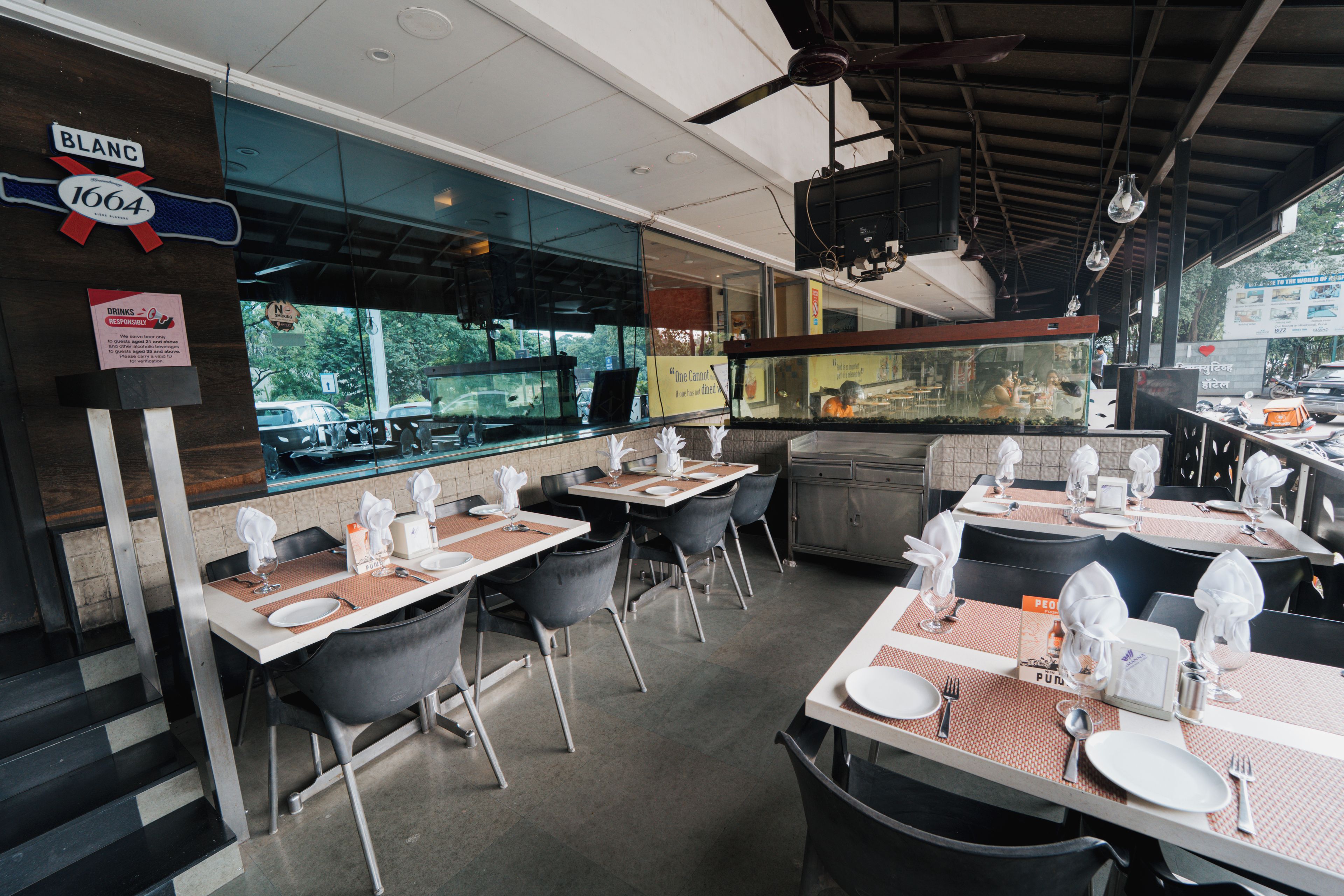 A restaurant interior with tables set for dining, a view through the window, and a sign indicating the establishment's name.