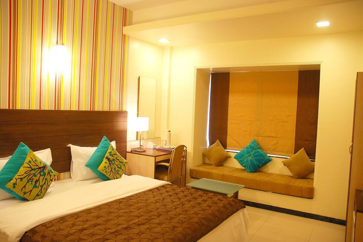 Habitación de hotel con una cama grande, un escritorio, una silla, un sofá pequeño y una ventana.